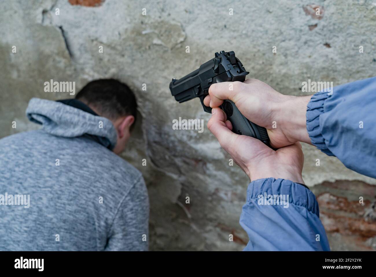 Primo piano a disposizione di un uomo sconosciuto terrorista o assassino tenendo una pistola puntò alla testa della vittima sconosciuta ostaggio con testa appoggiata contro un muro - te Foto Stock