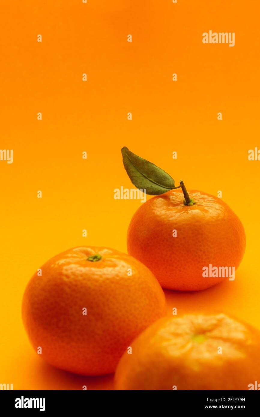 tre tangerini allineati a zig-zag su parte inferiore dell'immagine l'ultima ha una foto foglia verde su sfondo arancione e illuminazione a zenith Foto Stock