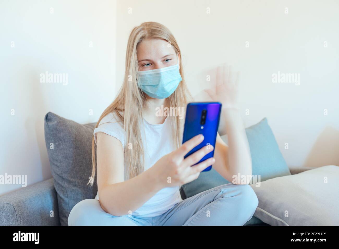 Bionda ragazza su un auto-isolamento e di una videochiamata con smartphone, indossando una maschera medica blu Foto Stock