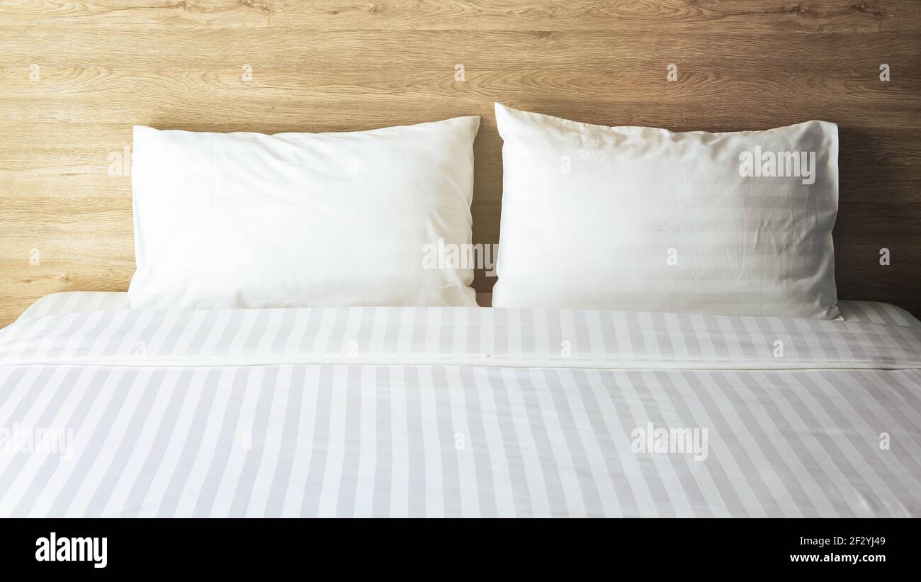 Camera con letto bianco, due cuscini bianchi, piumone bianco sul letto con testiera in legno e luce solare Foto Stock