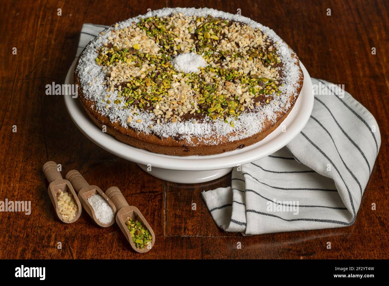 Dolce al cioccolato morbido con cocco, mandorla e pistacchio grani su stativo per torta bianca Foto Stock