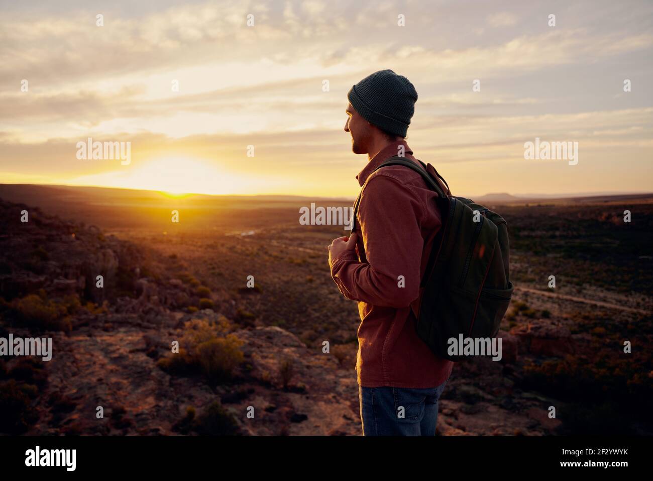Felice uomo turistico con zaino in piedi in cima alla montagna guardando in lontananza all'alba del mattino Foto Stock