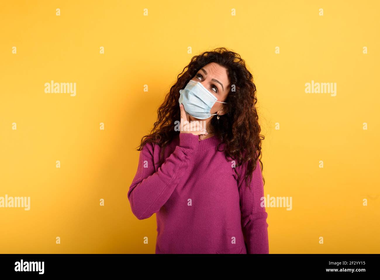 La donna ha dubbi sul virus della corona di covid19. Sfondo giallo. Foto Stock