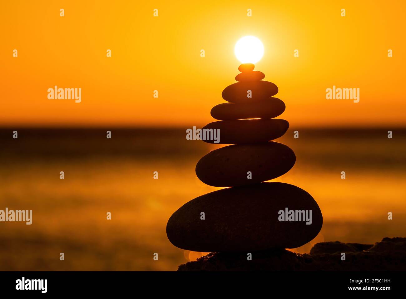 Profilo a piramide di ciottoli bilanciato sulla spiaggia. Astratto caldo tramonto bokeh con Mare sullo sfondo. Pietre Zen sulla spiaggia di mare, meditazione, spa Foto Stock