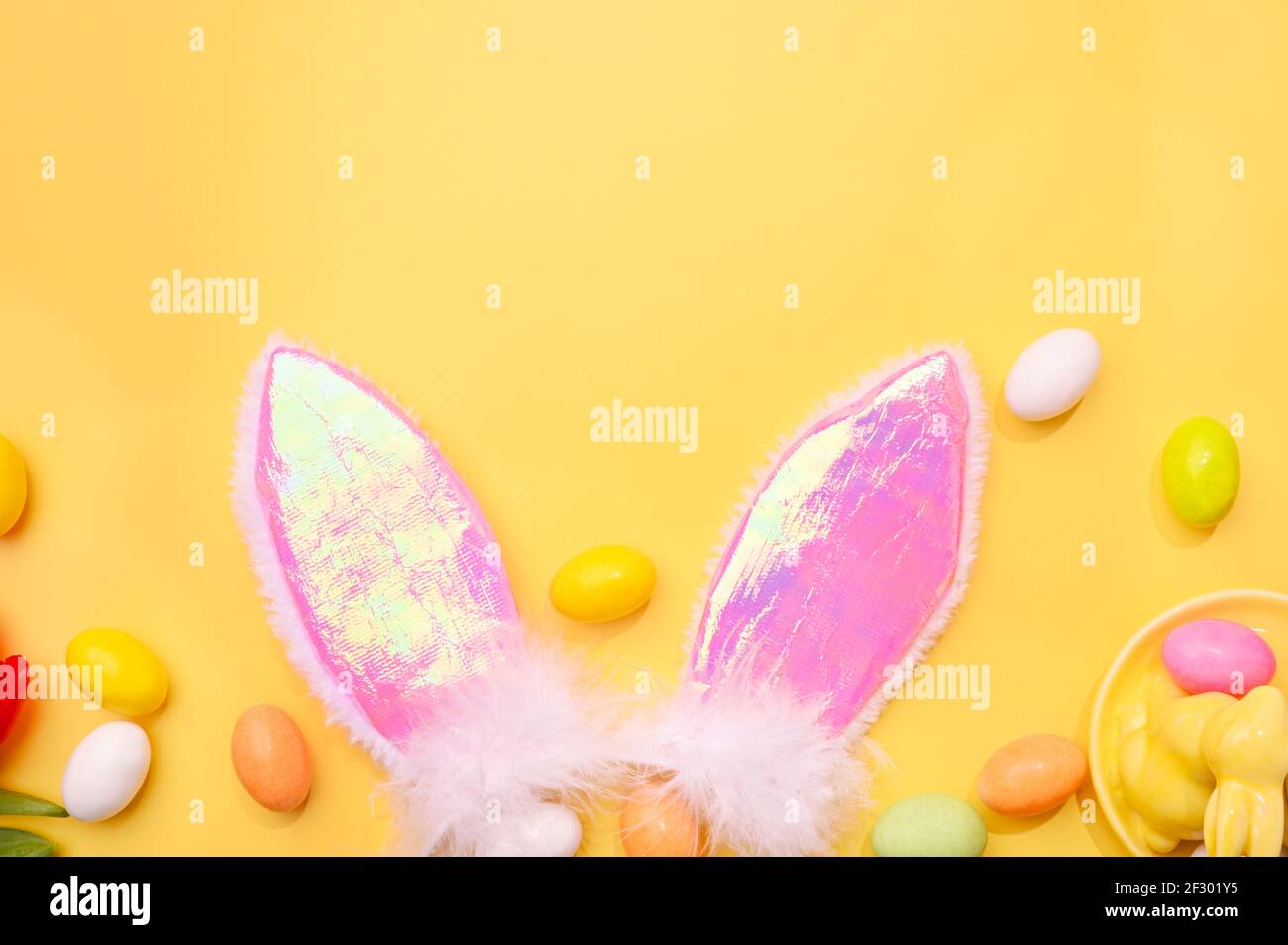 Molla. Uova di cioccolato di Pasqua, orecchie di coniglio rosa su sfondo giallo. Spazio libero per il testo. Spazio di copia. Formato banner lungo Foto Stock