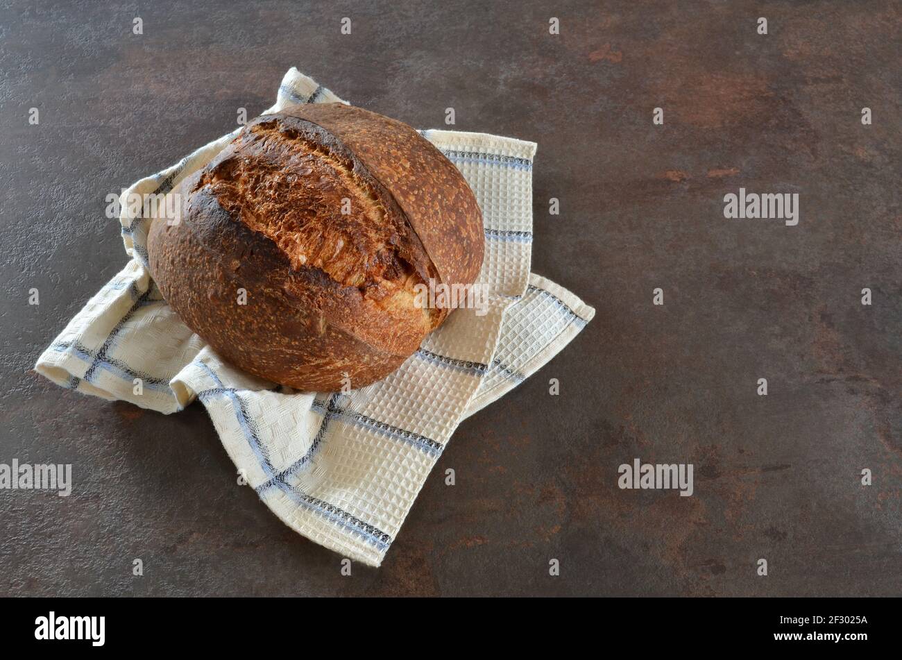 Pane appena sfornato di pane artigianale di segale su un asciugamano da cucina su uno sfondo scuro da vicino. Foto Stock