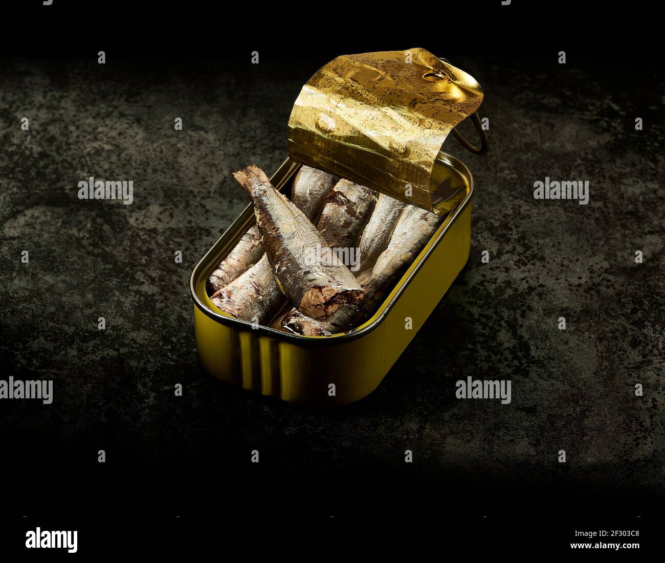 Una lattina gialla di sardine in olio d'oliva su un tavolo metallico invecchiato in un ambiente scuro. Foto Stock