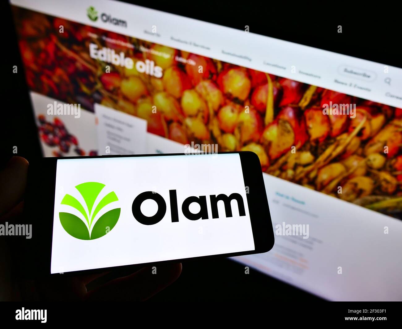 Persona che detiene il telefono cellulare con il logo della società agroalimentare Olam International Limited sullo schermo di fronte alla pagina web. Messa a fuoco sul display del telefono cellulare. Foto Stock