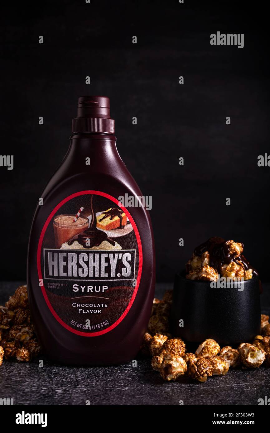messa a fuoco selettiva. lo sciroppo di cioccolato di hershey in una posizione verticale e a basso tasto. Con una tazza di popcorn al caramello condito con sciroppo di cioccolato Foto Stock