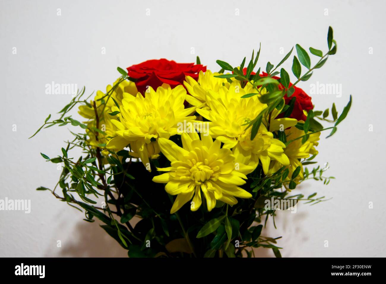 Un bouquet di fiori di rose rosse e crisantemi gialli senza imballaggio si trova in un vaso contro la parete bianca. I fiori sono grandi. Un dono, una dichiarazione d'amore. Vacanze. Foto Stock