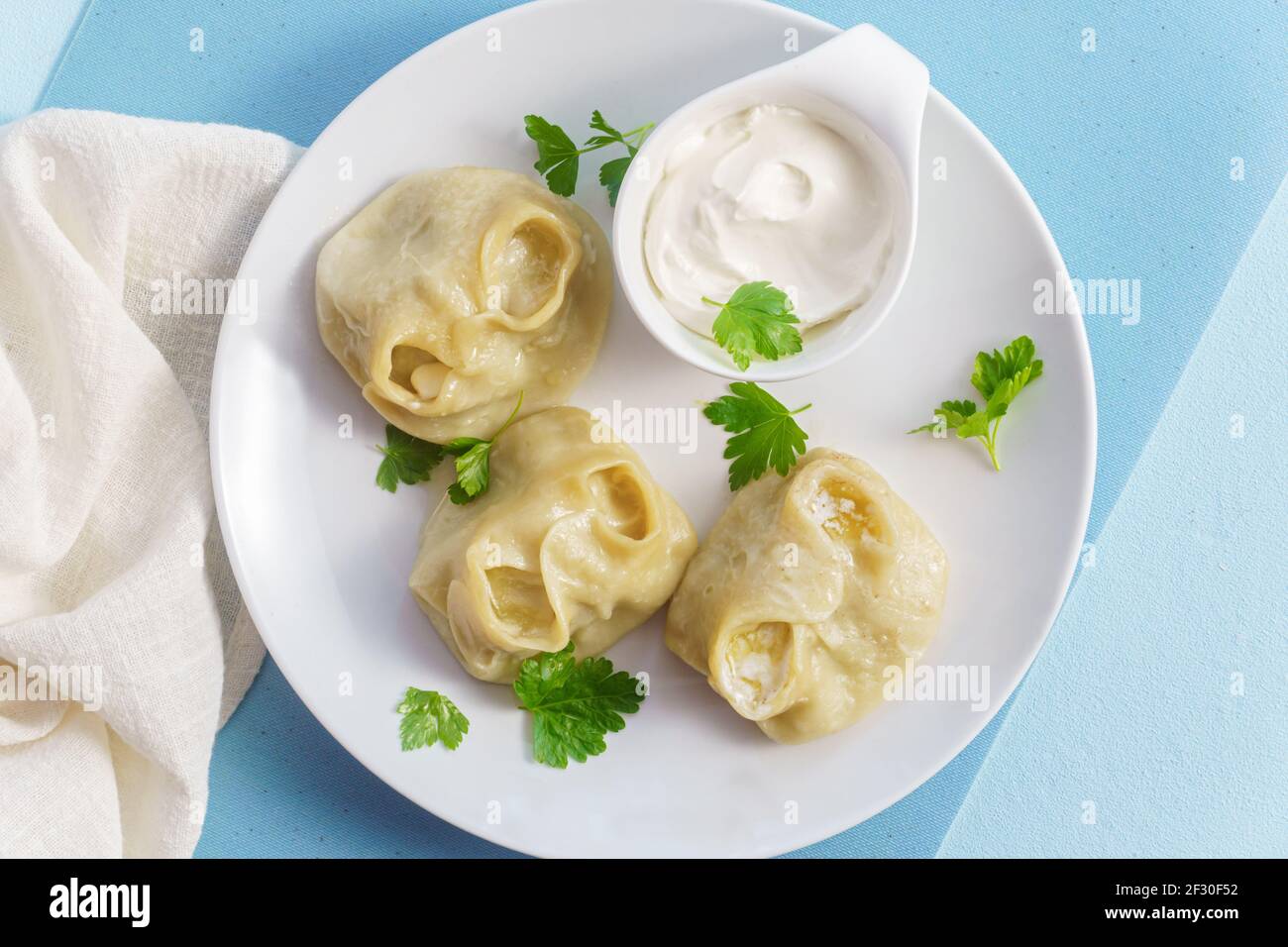 Cibo tradizionale manti su piatto con panna acida, gnocchi con carne macinata, cipolla e spezie. Vista dall'alto su blu Foto Stock