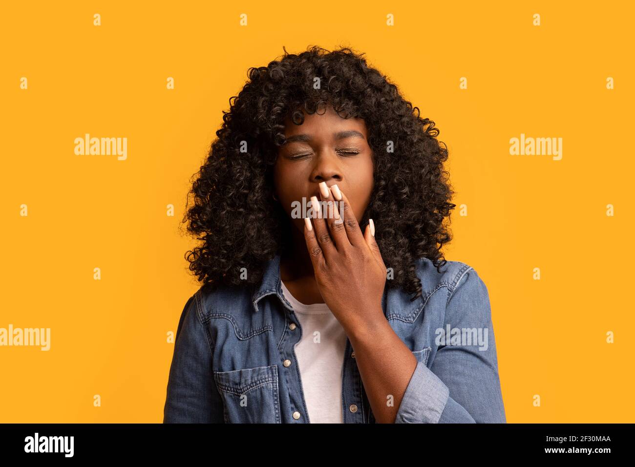 Donna afroamericana che brulica sul giallo, coprendo la bocca con la mano Foto Stock