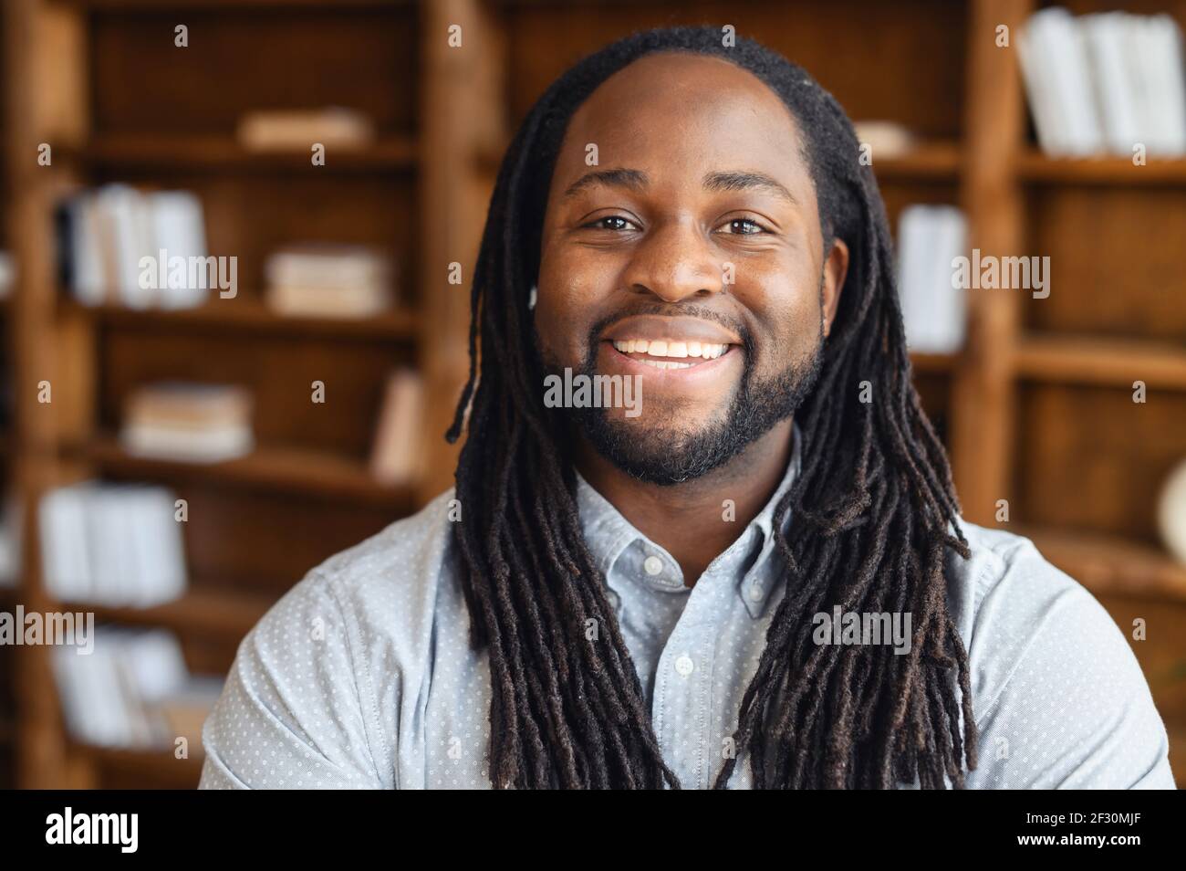 Ritratto primo piano di un giovane sorridente afroamericano con i temadlock in posa in biblioteca o guardando la macchina fotografica, l'ottimista direttore d'ufficio black man è pronto a lavorare Foto Stock