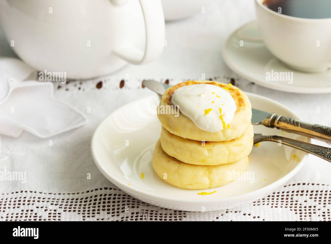 Frittelle al formaggio con panna acida e scorza di limone, servite con tè. Foto Stock