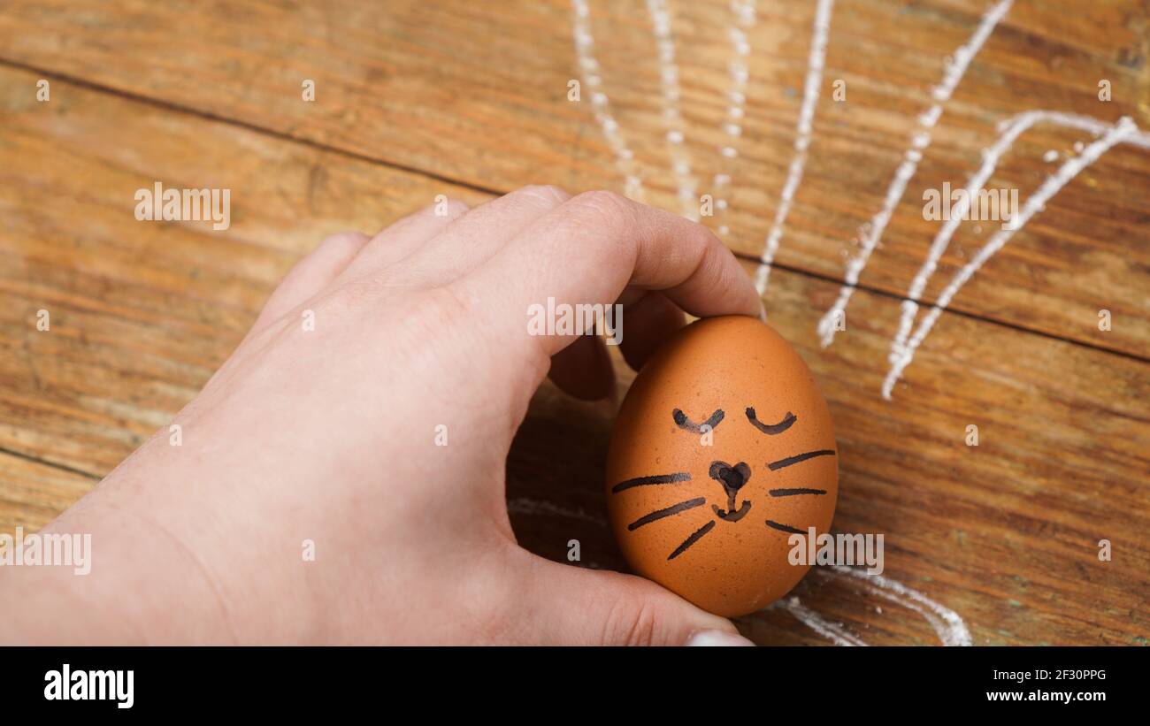 Una mano femminile tiene un uovo con un viso carino. Le orecchie sono disegnate con gesso Foto Stock