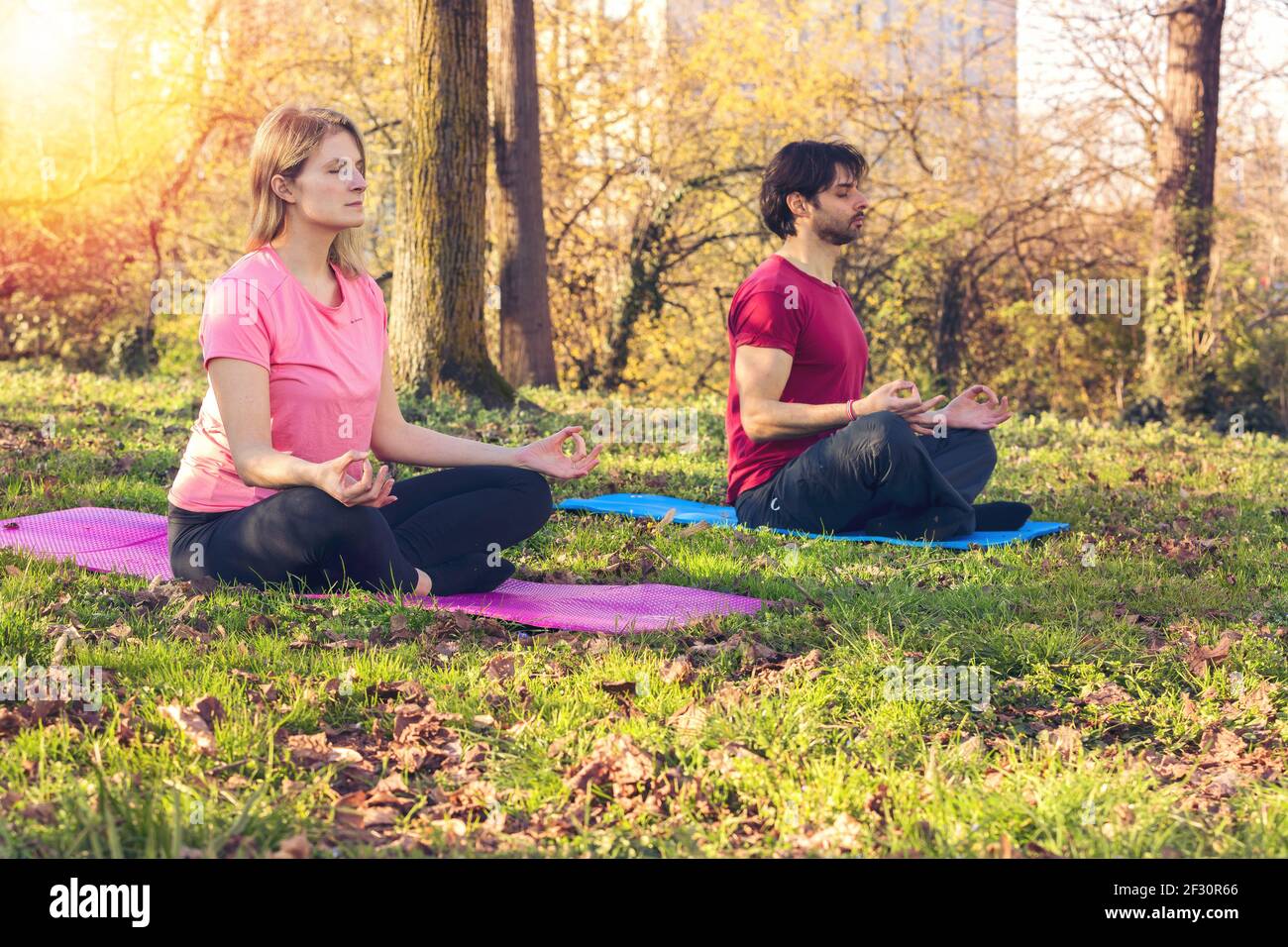 Lezione di yoga. Gioiosa gente pacifica seduta nel loto posa mentre si pratica yoga all'aperto Foto Stock