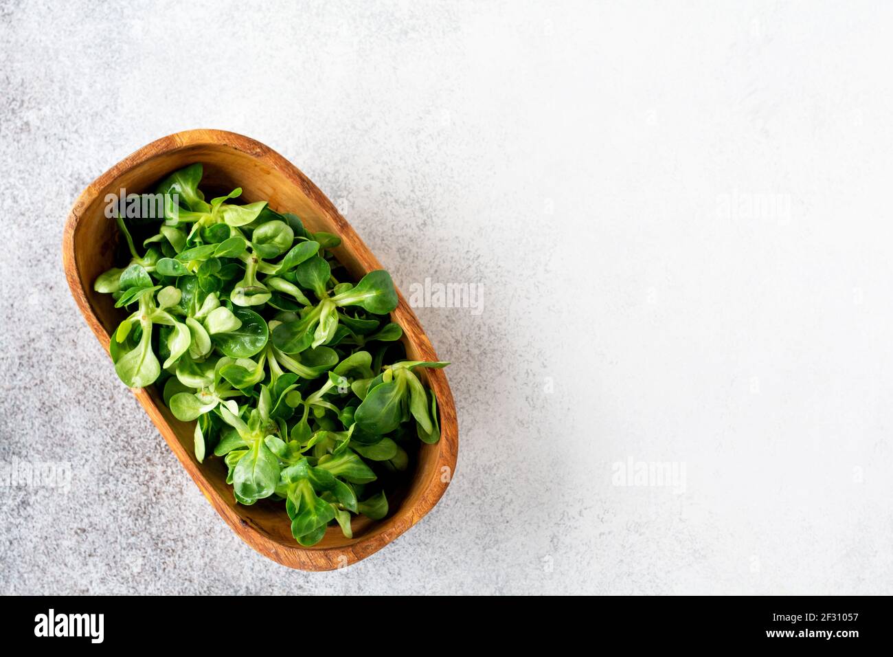 Insalata di cress fresca cruda in ciotola di olive di legno su uno sfondo di pietra chiaro. Messa a fuoco selettiva. Vista dall'alto. Posiziona per il testo Foto Stock
