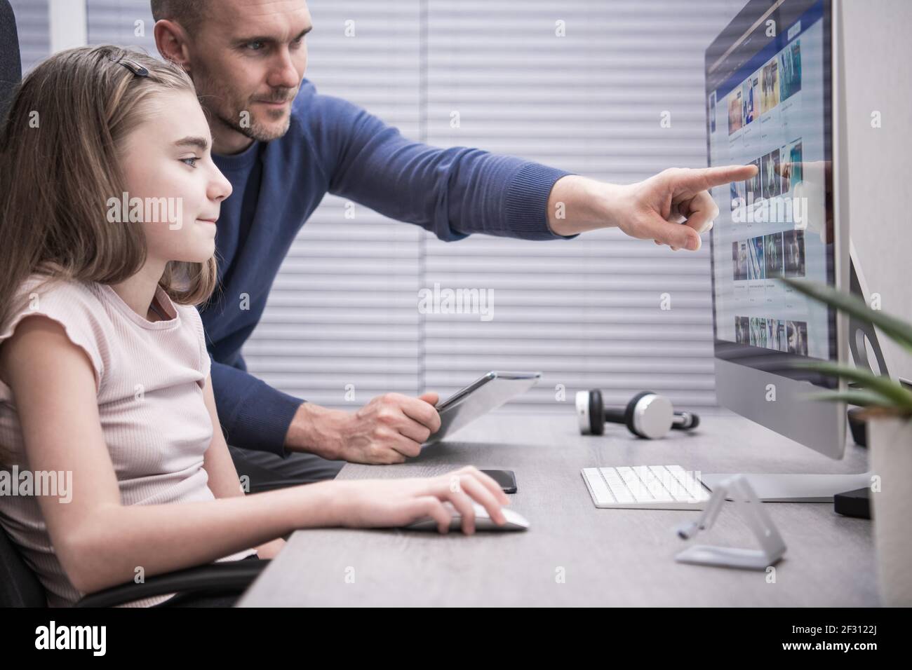 Padre caucasico nei suoi 40 anni e sua figlia che lavora al progetto scolastico davanti al computer desktop. Uomini che puntano qualcosa con il dito sul desktop Foto Stock