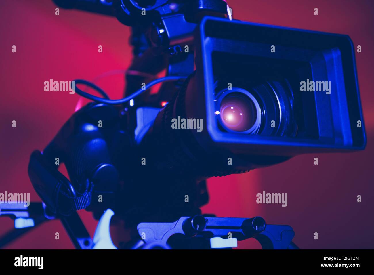 Moderna fotocamera digitale per cinema con teleobiettivo Moto Zoom collegato in primo piano con illuminazione scenografica blu e rossa. Apparecchiature per l'industria cinematografica. Foto Stock