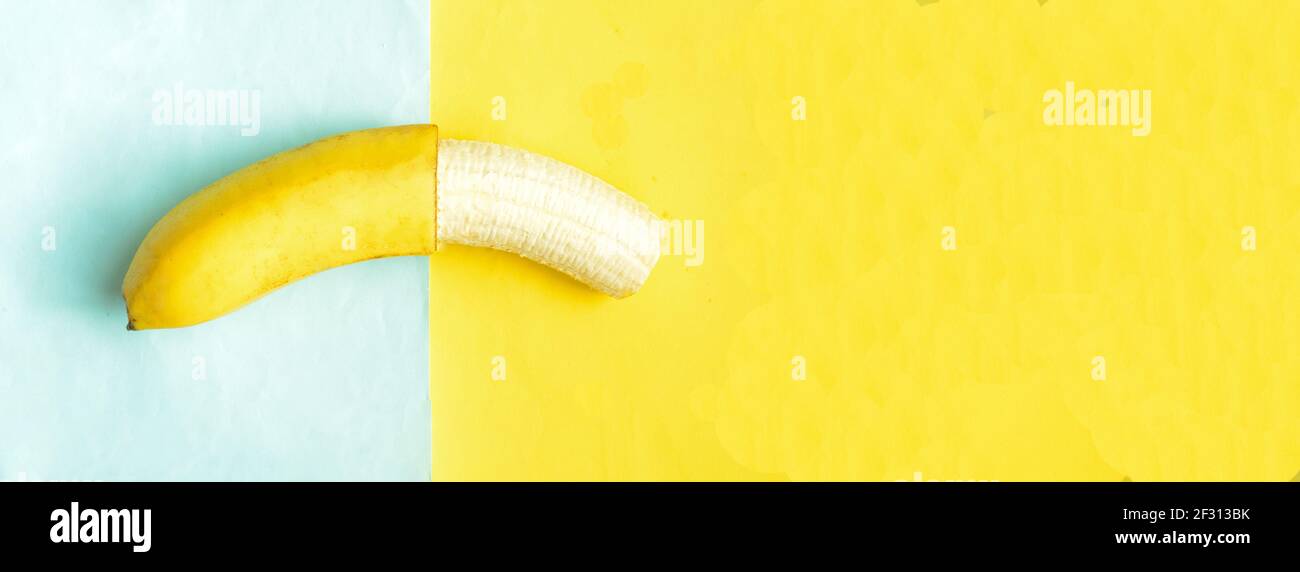 Una banana parzialmente sbucciata su fondo giallo blu, Foto Stock