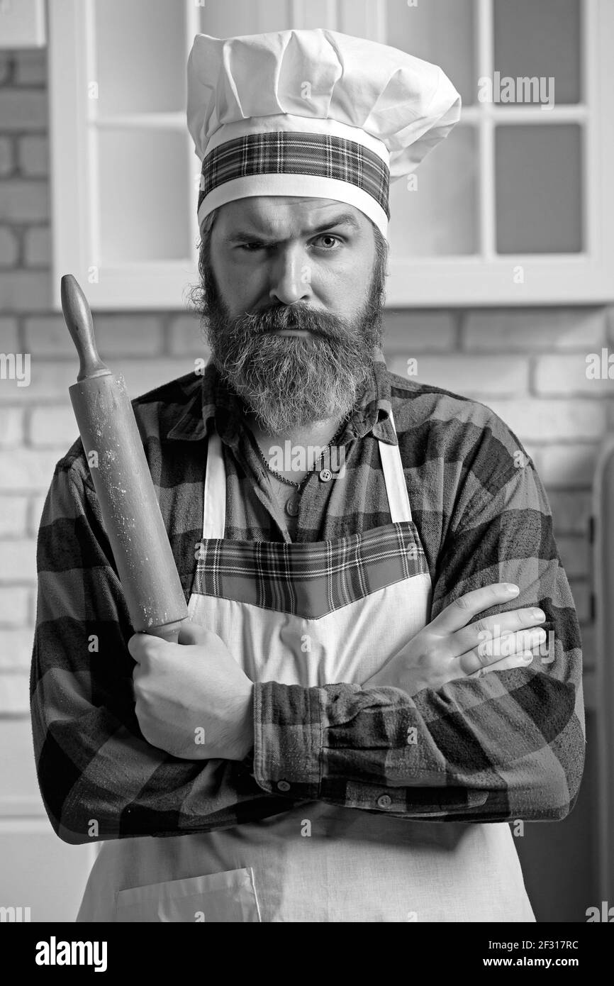 Cuoco arrabbiato in un grembiule con un tondino, un ritratto sullo sfondo della cucina Foto Stock