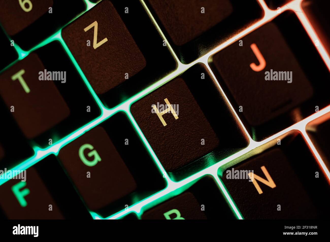 Macro closeup di tasti verdi gialli illuminati della tastiera del computer (Mettere a fuoco la lettera H) Foto Stock