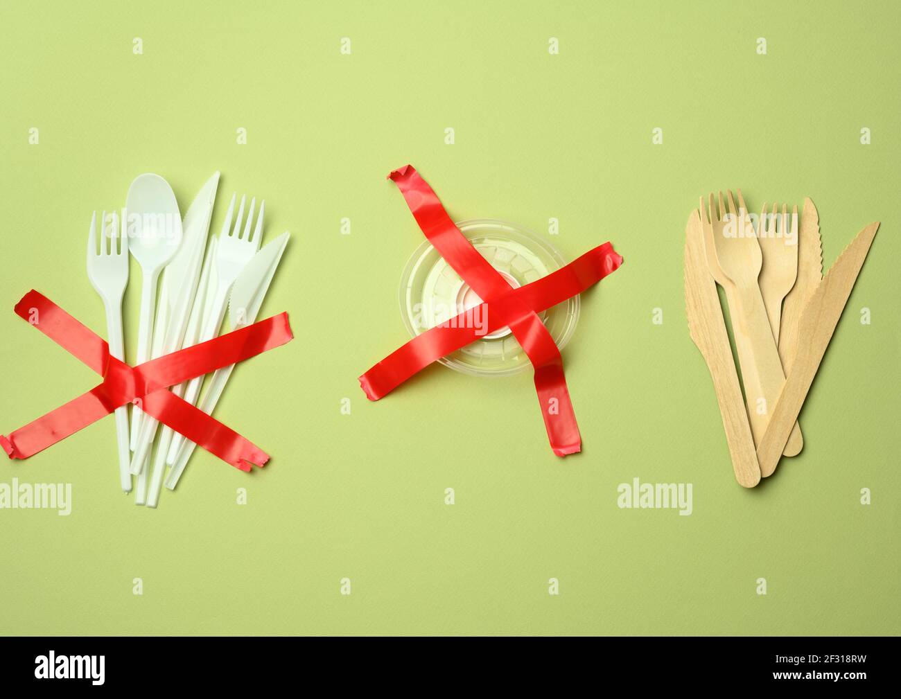 Forcelle e cucchiai in plastica incollati con nastro rosso su fondo verde, evitando la plastica Foto Stock