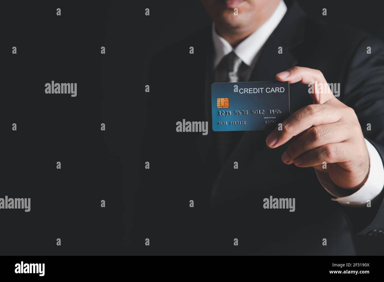 uomo d'affari in costume nero e cravatta grigia con carta di credito su sfondo nero. Concetto di Payment Banking Foto Stock