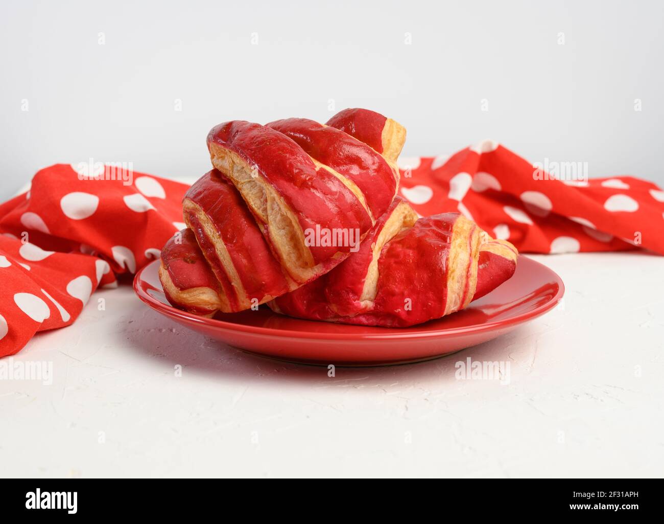 Due croissant al forno con glassa di ciliegia su ceramica rossa piastra Foto Stock