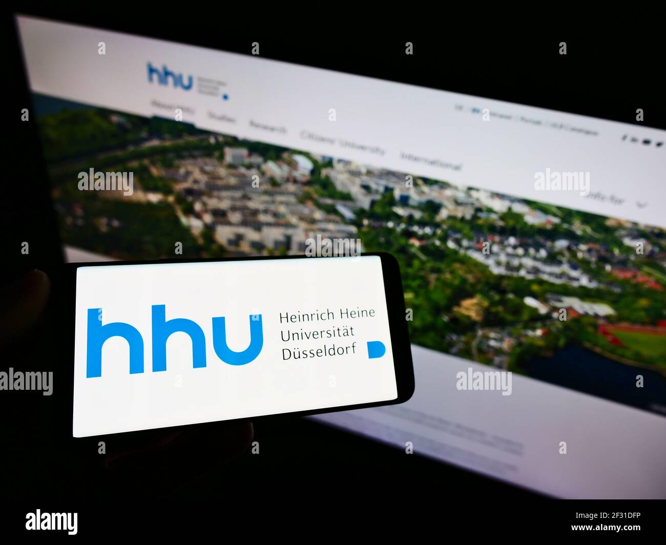 Persona in possesso di smartphone con logo tedesco Heinrich-Heine-Universität Düsseldorf (HHU) sullo schermo davanti al sito web. Mettere a fuoco il display del telefono. Foto Stock