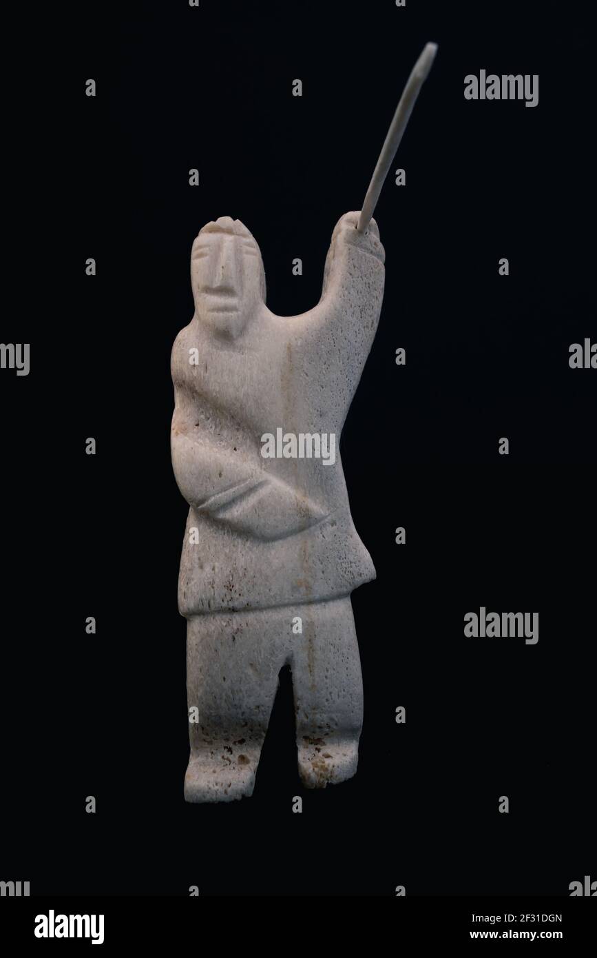 Piccola statua del cacciatore inuit con una lancia fatta di osso animale. Isolato su sfondo nero. Arte inuit Cultura tribale dei nativi nell'estremo nord Foto Stock