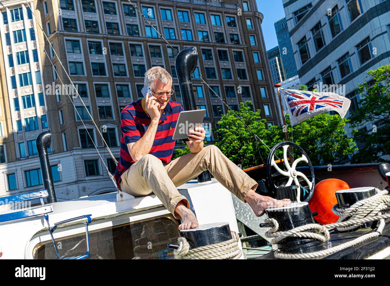 Casa ufficio uomo d'affari maturo fuori casa barca ufficio parlare su smartphone guardando il tablet computer Canary Wharf uffici dietro Londra E14 Foto Stock Casa ufficio uomo d'affari maturo fuori casa barca ufficio parlare su smartphone guardando il tablet computer Canary Wharf uffici dietro Londra E14 Foto Stock