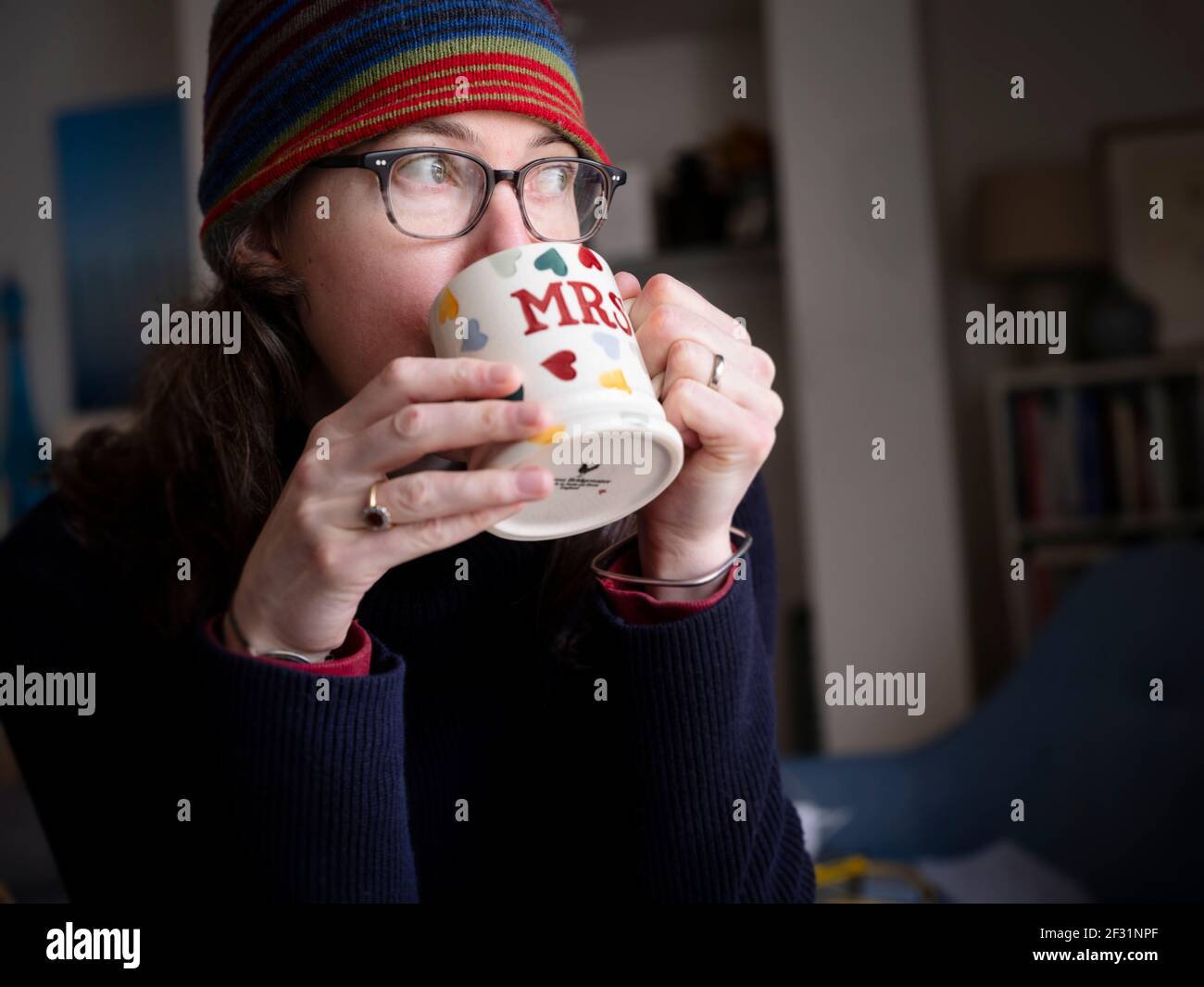 Una donna di mezza età che indossa un cappello a maglia da una tazza decorata con cuori e 'mrs' sul lato. Foto Stock