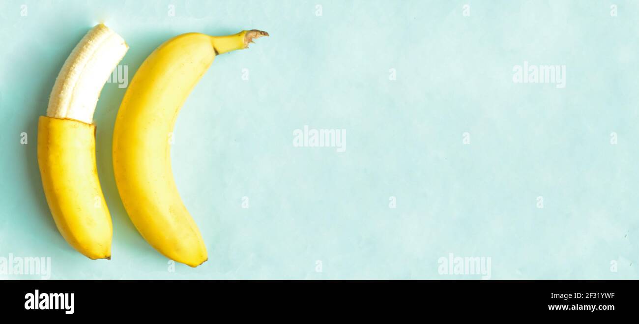 Una banana parzialmente sbucciata e una intera su sfondo blu. Foto Stock