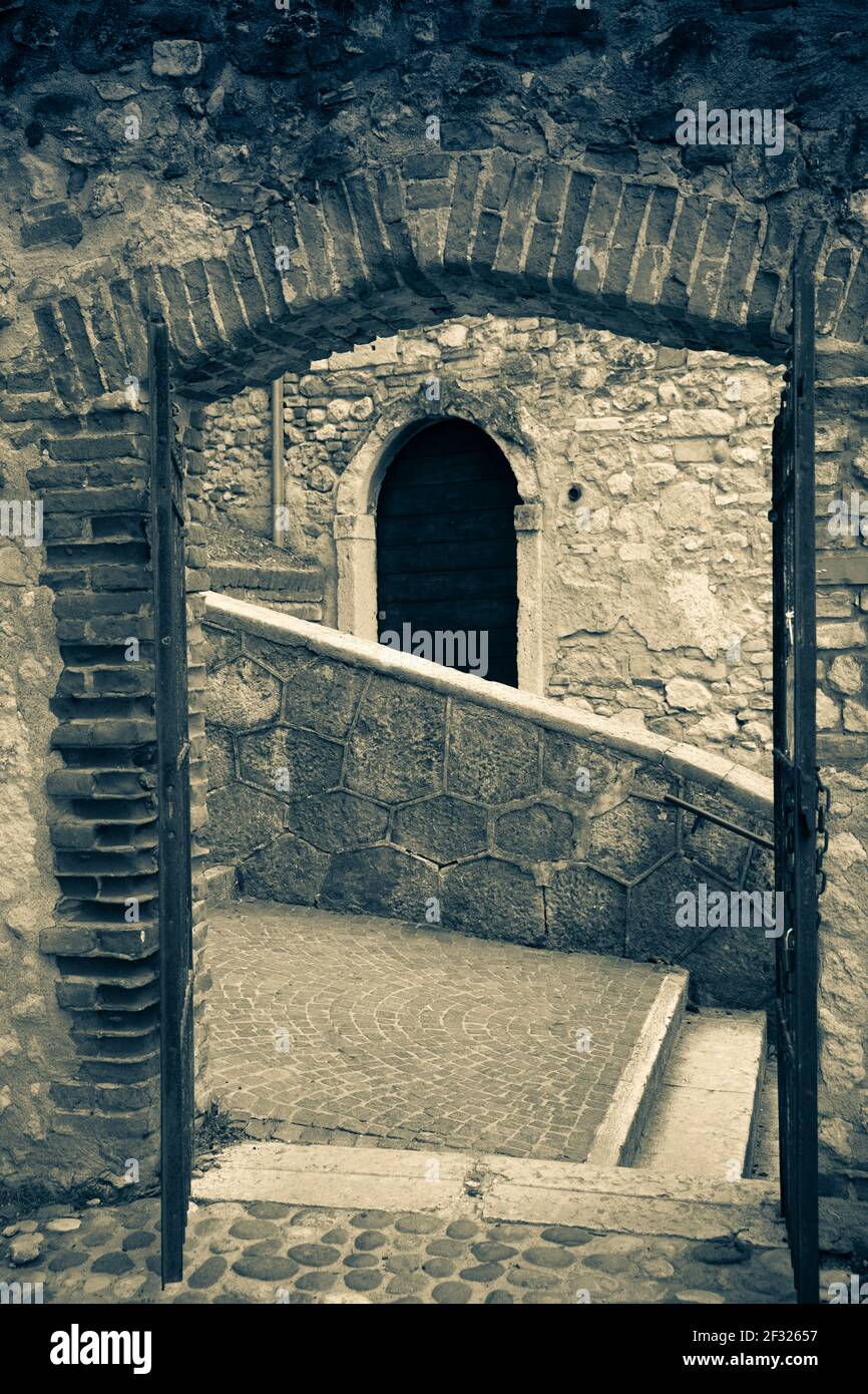 Italia, Verona, immagine in bianco e nero di una strada che mostra l'apertura di una porta, marciapiede e muro di pietra Foto Stock