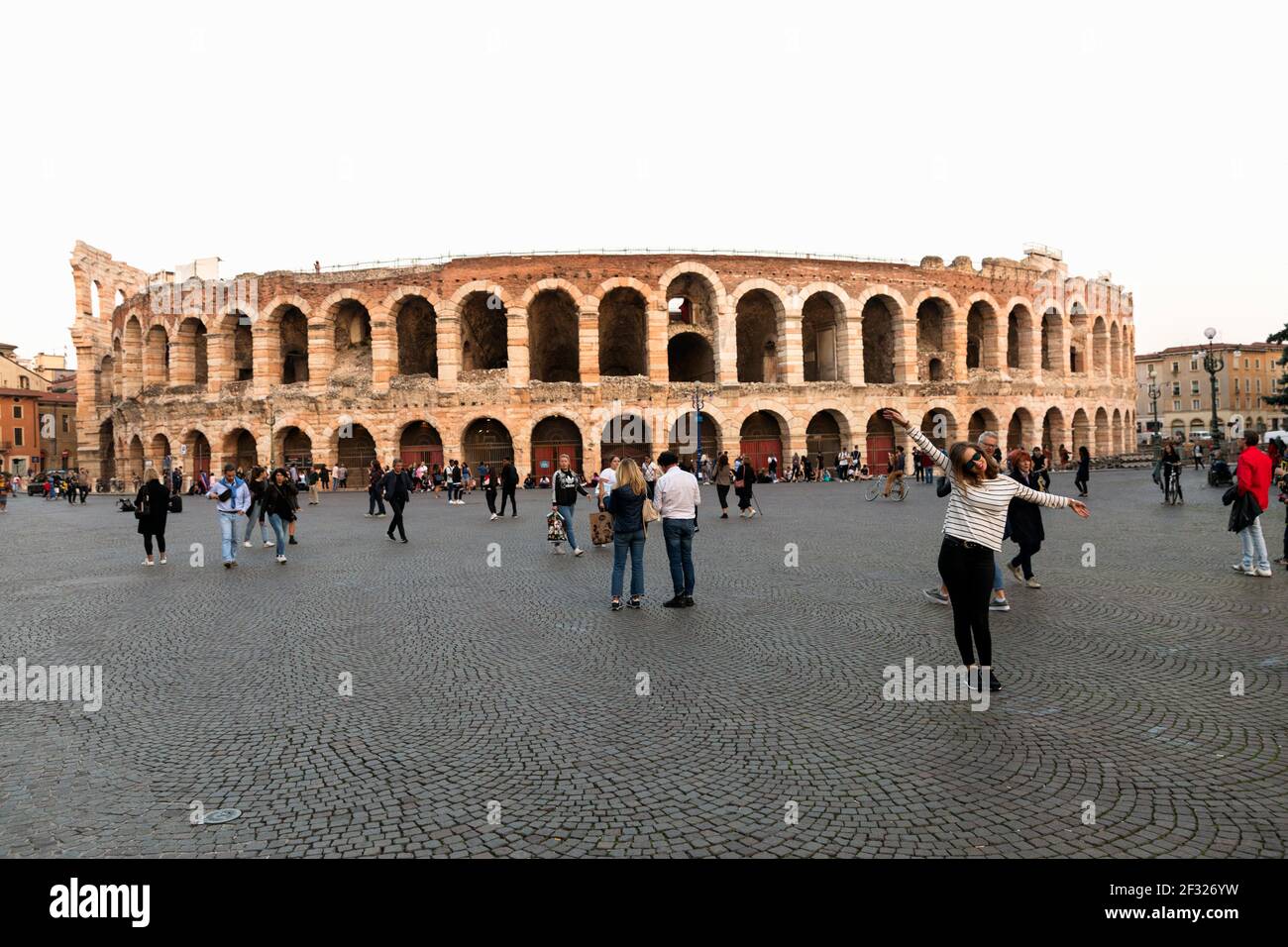 Italia, Verona, turisti che si posano in Piazza Bra con l'Arena o l'Anfiteatro di Verona nel retrocoperto. Foto Stock
