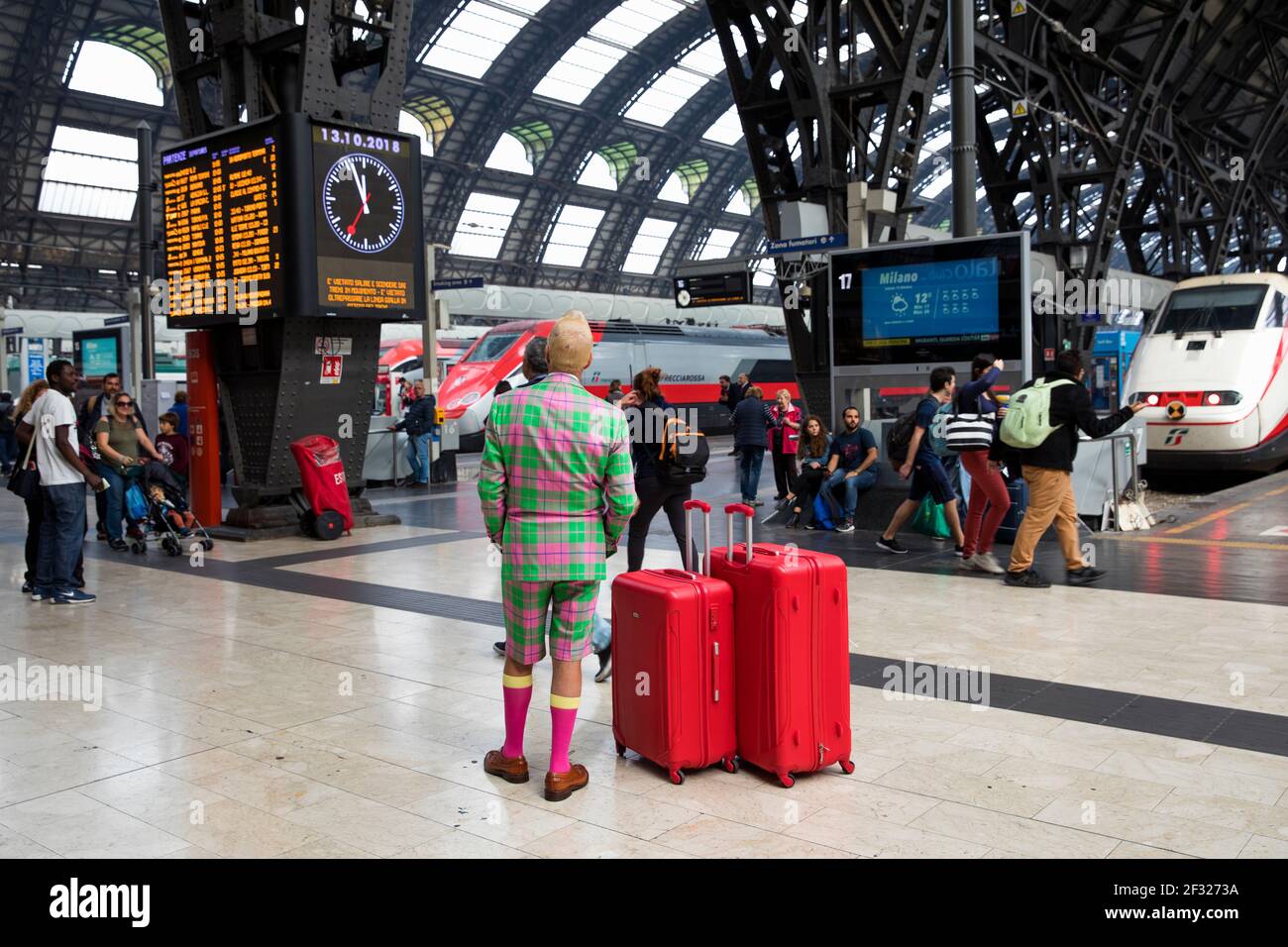 Italia, Milano, Stazione ferroviaria di Milano, uomo colorato con bagagli rosso brillante in attesa di un treno Foto Stock