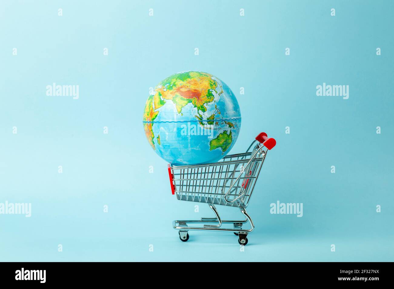 Mondo vendita e vendita via Internet concetto. Carrello per supermercati con globo terrestre su sfondo blu. Il commercio mondiale e la consegna degli acquisti. Foto Stock