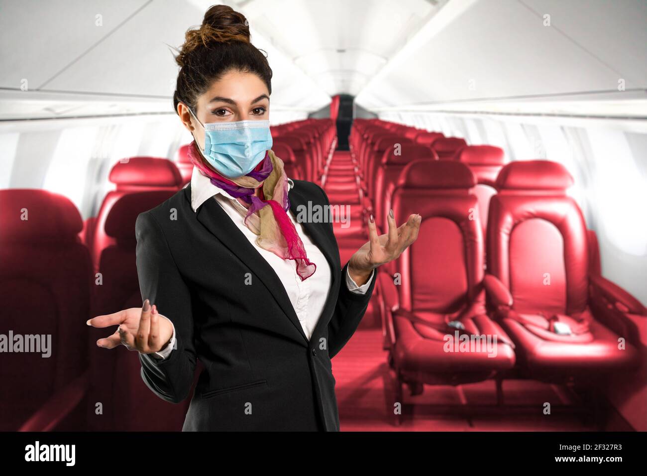 Un bellissimo assistente di volo con sciarpa multicolore e maschera, illustra l'interno di un aereo. Scatto perfetto per viaggi, vacanze e lavoro Foto Stock