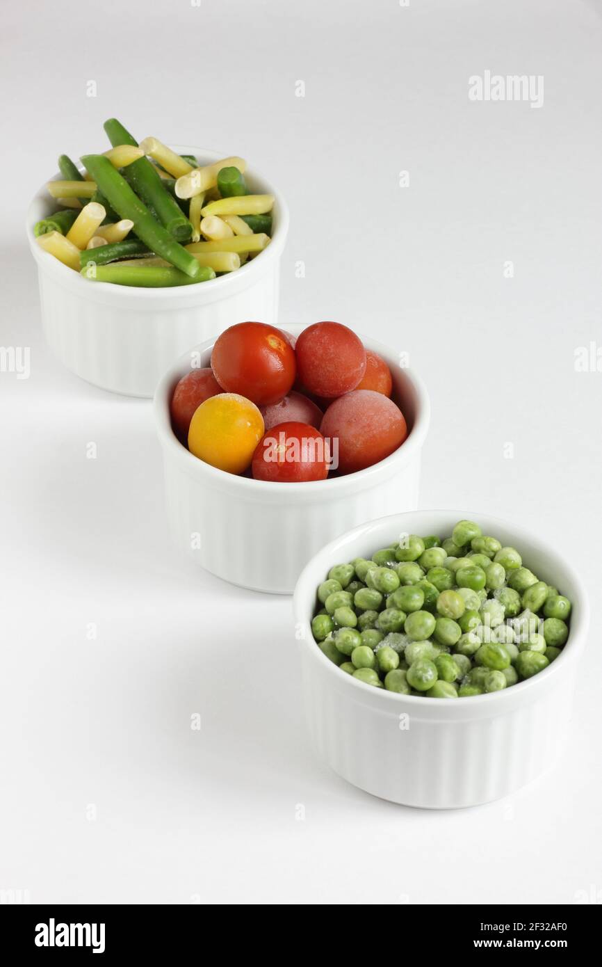 Verdure surgelate assortite in ciotole isolate su sfondo bianco, closeup, conservando i avanzi, concetto di deposito di cibo e mangiando i pasti nel concetto domestico Foto Stock