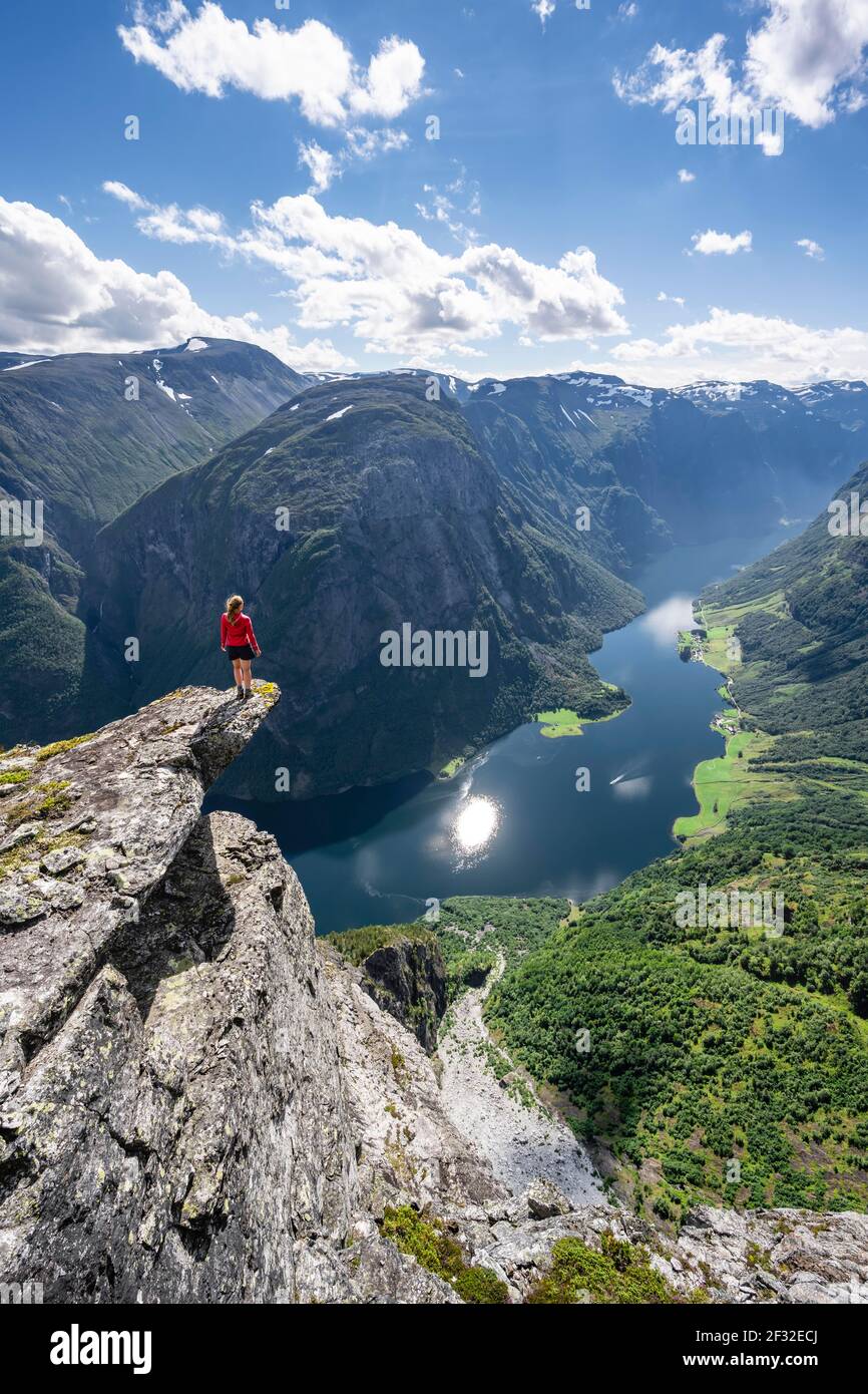 Escursionista in piedi su affioramento roccioso, vista dalla cima di Breiskrednosi, montagne e fiordo, Naeroyfjord, Aurland, Norvegia Foto Stock