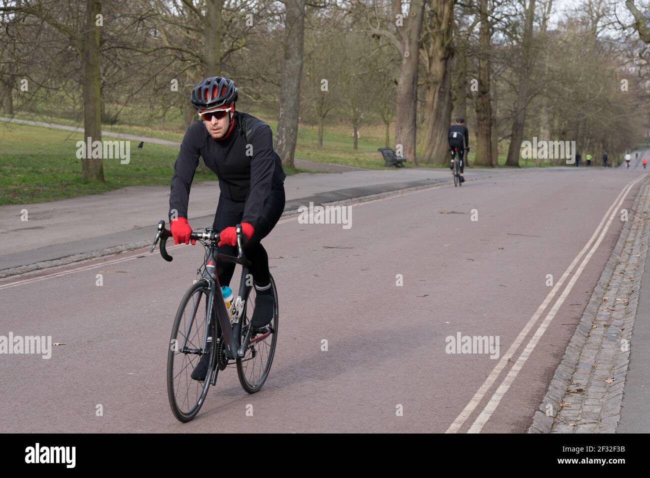 Ciclista maschile in guanti rossi e occhiali da sole neri con casco cavalcare in salita a Londra Greenwich Park, Regno Unito Foto Stock