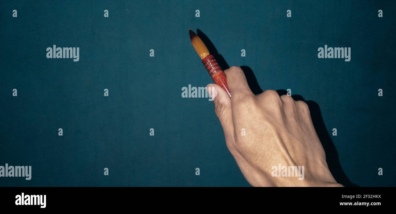 mano tenendo un lungo pennello acquerello su tela blu, preparando un dipinto, soggetto isolato. Foto Stock