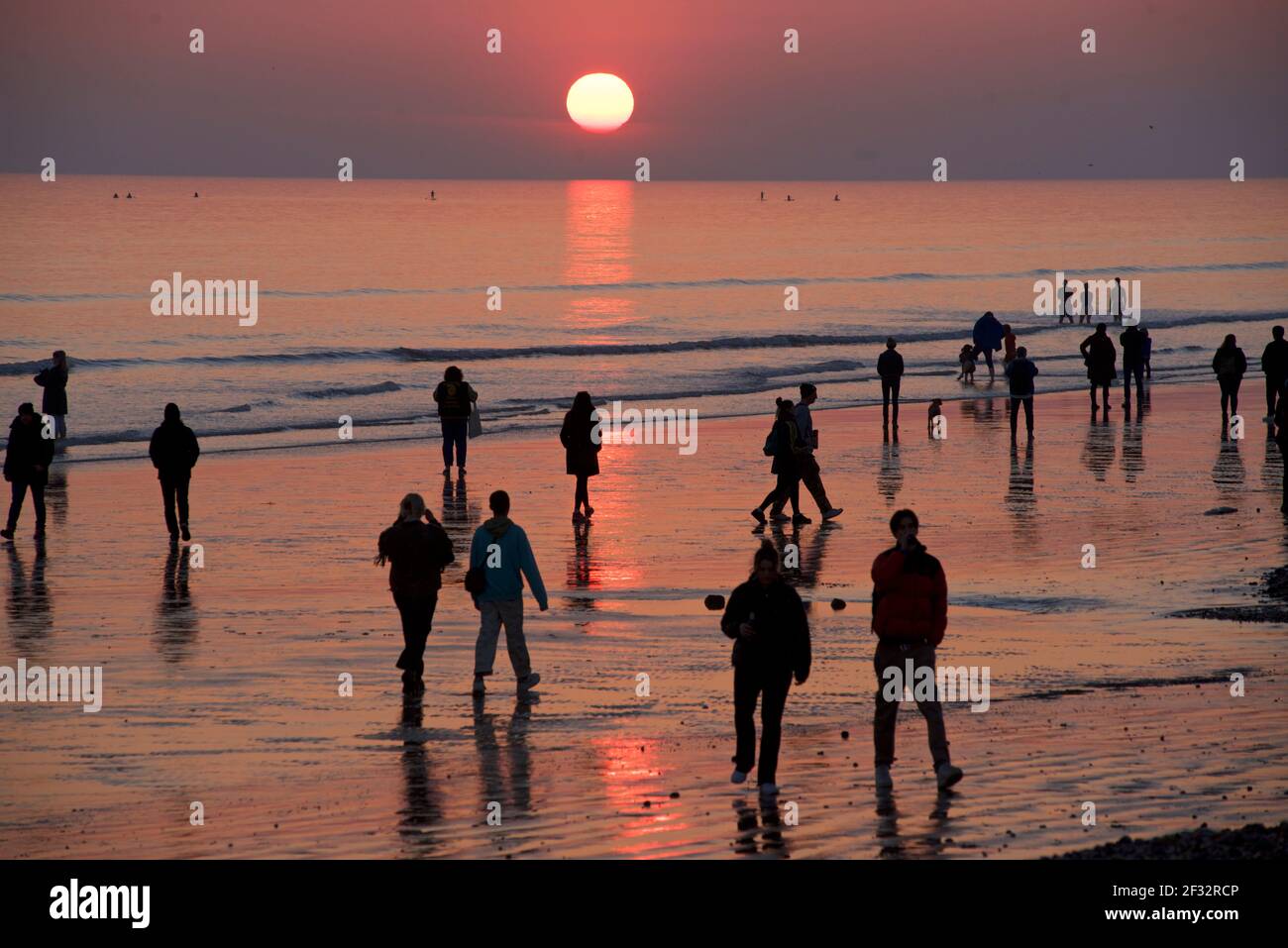 Spiaggia di Brighton e Hove a bassa marea. Sagome di persone che camminano lungo la spiaggia sabbiosa al tramonto. East Sussex, Inghilterra Foto Stock