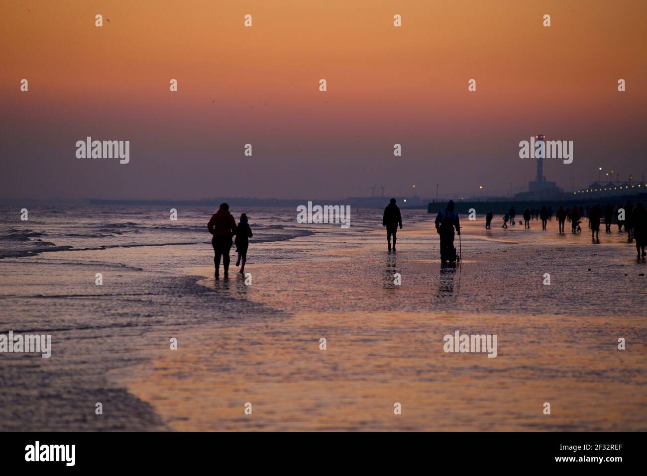 Spiaggia di Brighton e Hove con bassa marea che guarda ad ovest. Sagome di persone che camminano lungo la riva al tramonto. East Sussex, Inghilterra Foto Stock