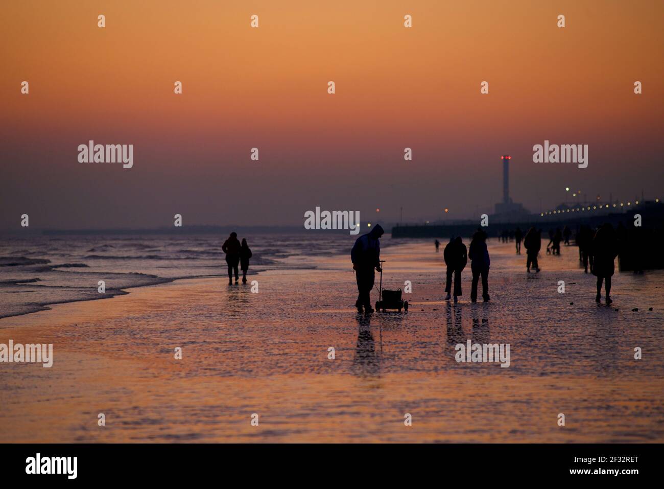 Spiaggia di Brighton e Hove con bassa marea che guarda ad ovest. Sagome di persone che camminano lungo la riva al tramonto. Pescatore che raccoglie vermi per pesca esca. Sussex, Inghilterra. Foto Stock
