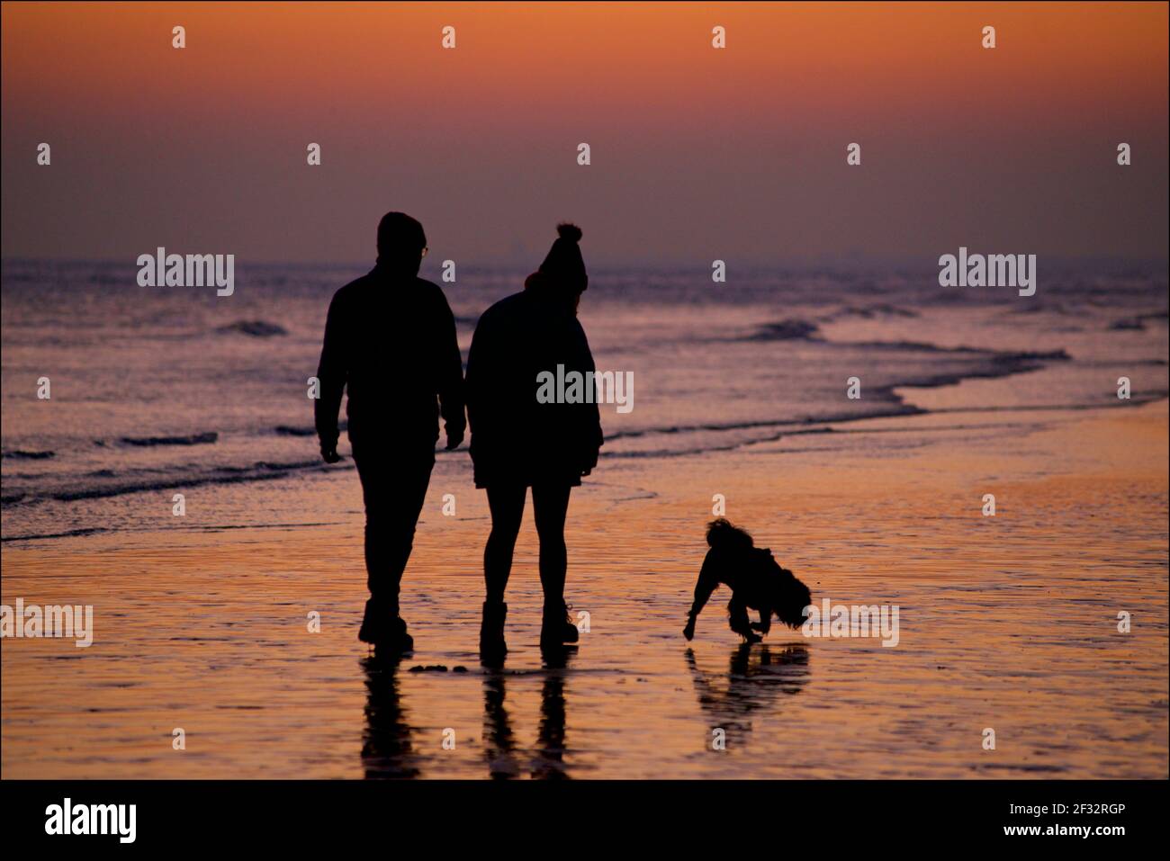 Spiaggia di Brighton e Hove con bassa marea che guarda ad ovest. Silhouette di coppia che camminano lungo la riva al tramonto. Con un cane. East Sussex, Inghilterra, Regno Unito. Foto Stock