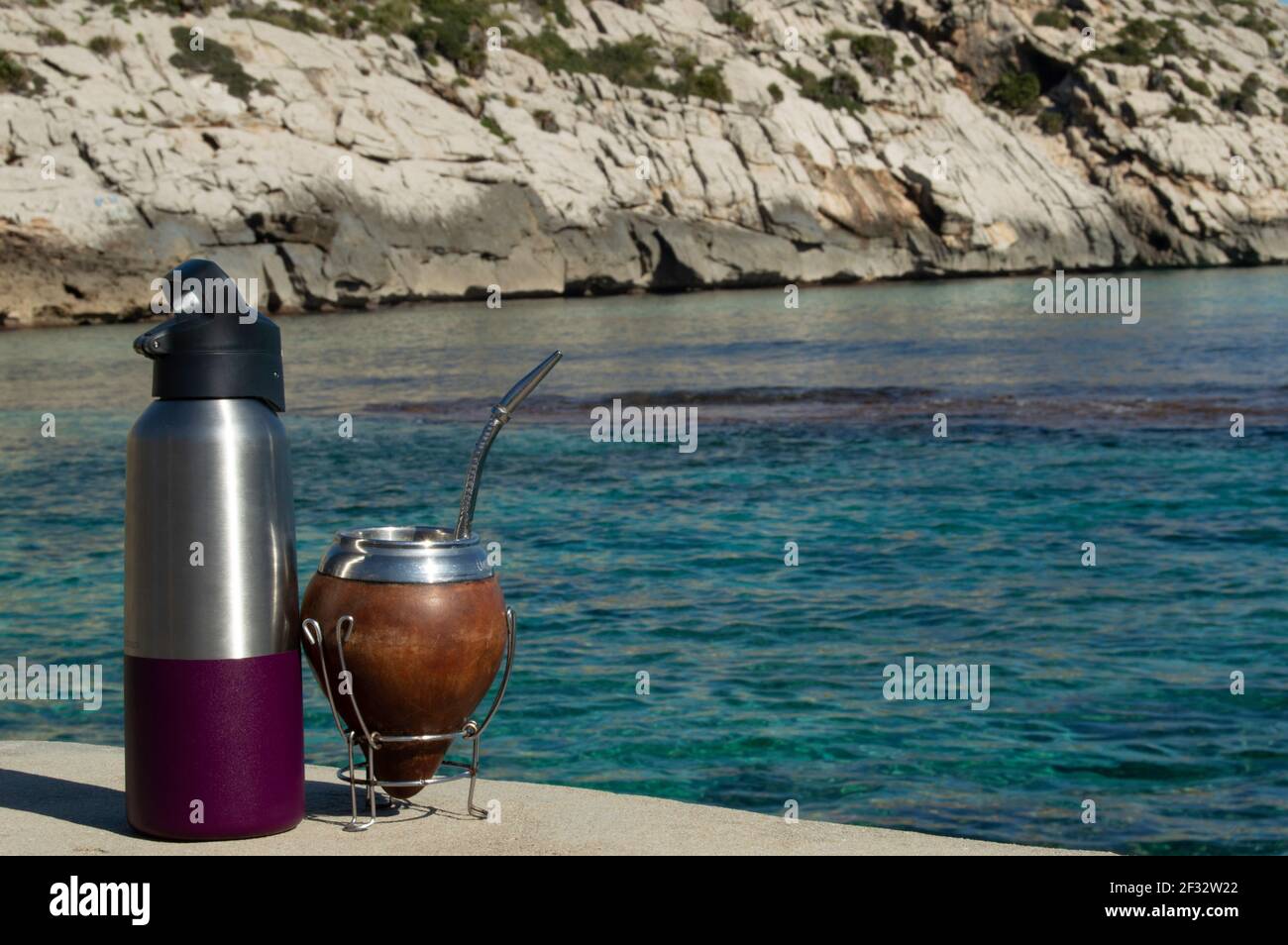 Mate y termo en la playa- bere Mate sulle rocce. Spiaggia mediterranea con acque turqoise trasparenti. Buona sensazione. Stile di vita Helthy Foto Stock