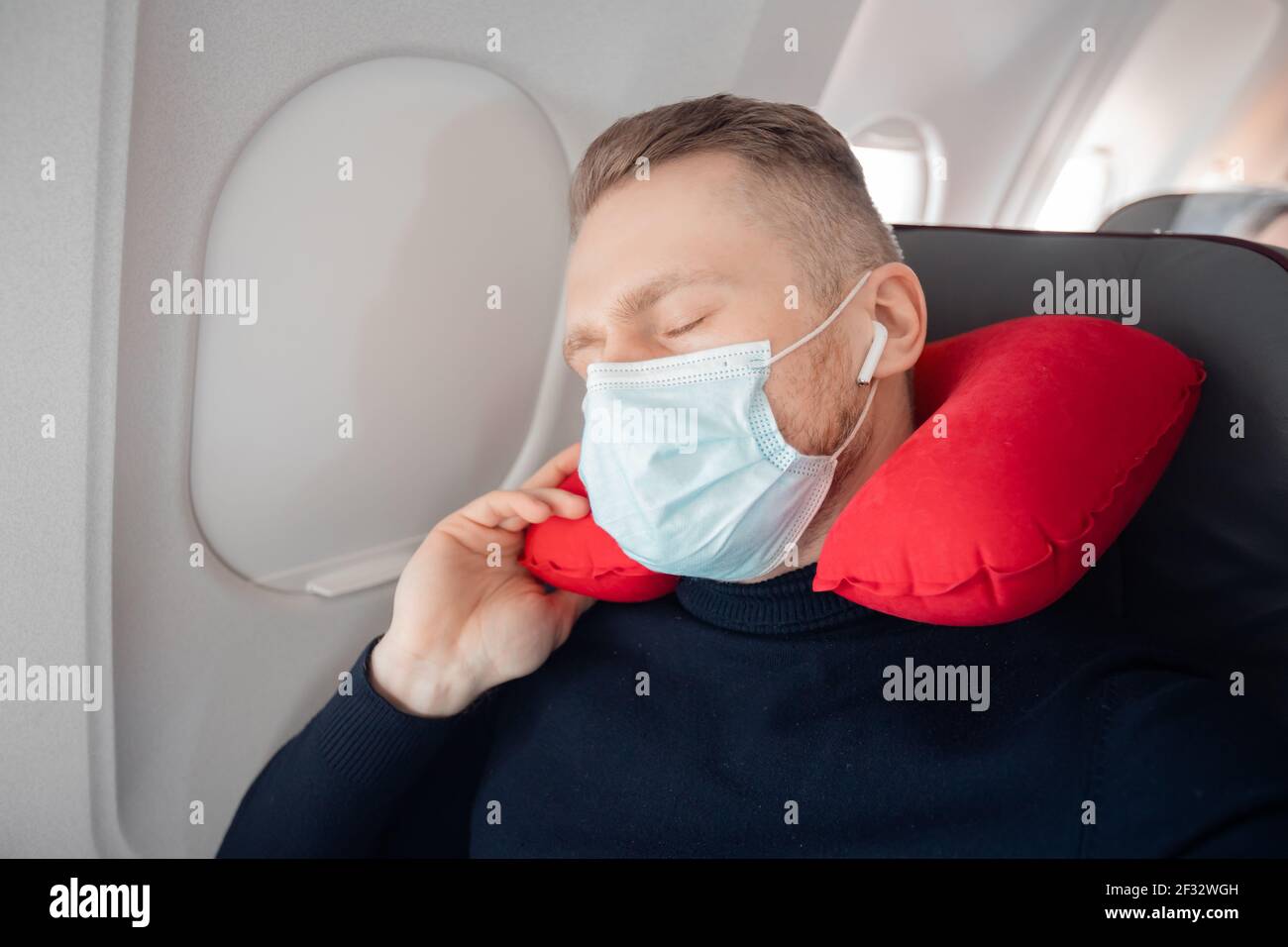 Il passeggero maschile dell'aereo ascolta la musica e gode di un cuscino per  dormire in sedia. Concetto di viaggio con maschera di sicurezza Foto stock  - Alamy