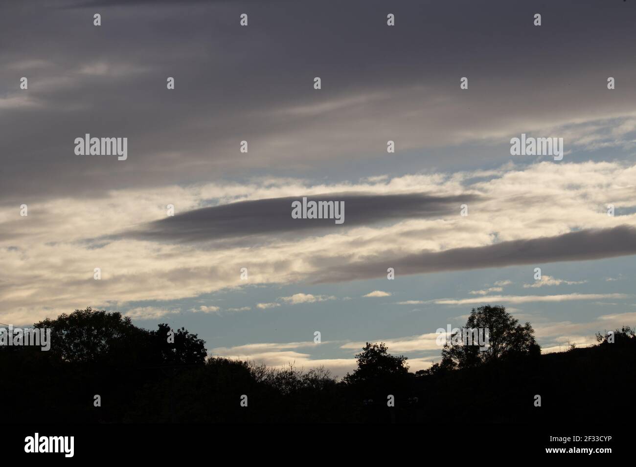 silhouette di alberi e una collina contro le nuvole e. cielo blu di sera Foto Stock